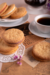 photo Assorted crispy sandwich biscuits and hot coffee offer a cozy experience with sweet fillings surrounded by classic vintage newspaper and delicate flowers