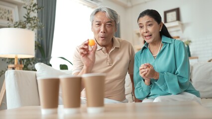 Obraz premium Happy elderly couple enjoying a ball toss game together at home, practicing coordination and cognitive skills for healthy aging. Grandfather and grandmother throwing ping pong in the bowl. Myrmidon.
