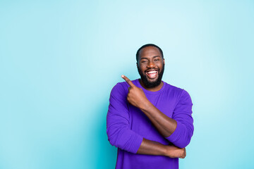 Photo of attractive dark skin business guy toothy smiling indicating finger to empty space advising amazing sales wear casual orange pullover isolated blue color background
