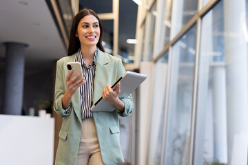 Confident Latina businesswoman multitasking with a smartphone in an office
