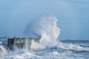 À Lesconil, les vagues déchaînées frappent la jetée sous un ciel bleu. L'écume éclatante...