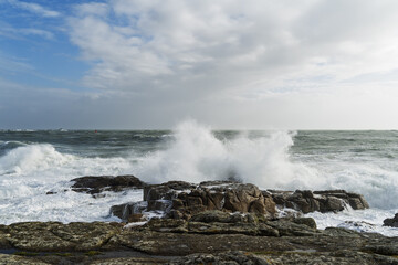 L’océan déchaîné à Lesconil, Bretagne, avec des vagues imposantes se brisant contre les rochers sous un ciel légèrement bleu en hiver.