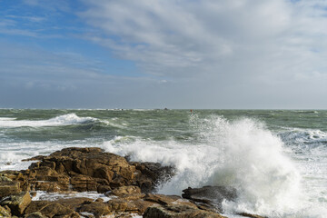 Mer agitée à Lesconil, Bretagne, les vagues frappent les rochers, sous un ciel partiellement bleu...