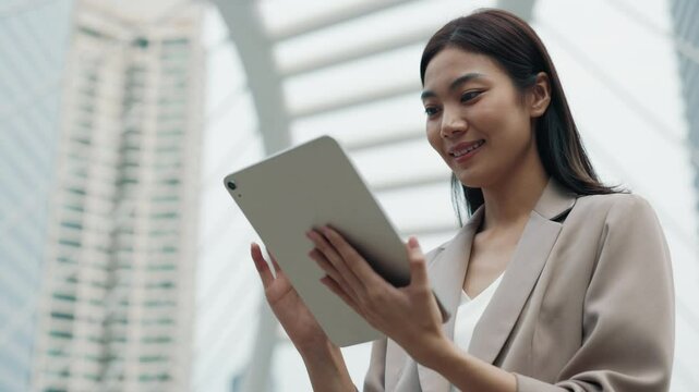 Portrait of happy Thai female manager browsing internet using tablet on street.