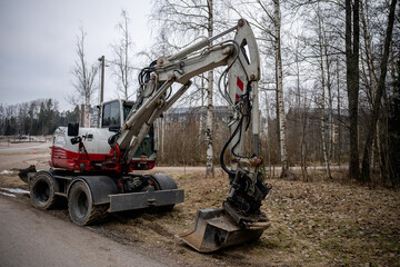 Large wheeled excavator with hydraulic arm and bucket on muddy ground near a forest.	
