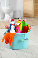 Bucket with different cleaning supplies on floor in bathroom