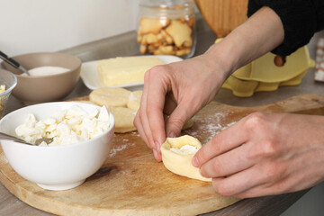 Woman making pirozhki (stuffed pastry pies) with cottage cheese at table, closeup