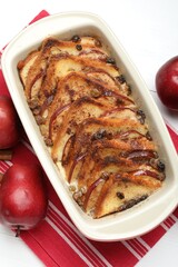 Delicious bread pudding in baking dish and fresh apples on white table, flat lay