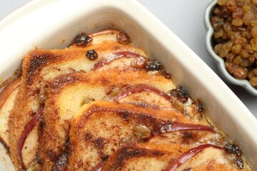 Delicious bread pudding in baking dish and raisins on light gray table, closeup