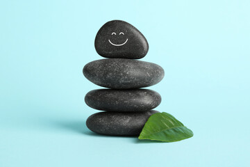 Stack of rocks with drawn smiley face on light blue background. Harmony and life balance