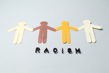 Word Racism and human paper figures of different colors on light grey background, closeup