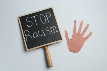 Chalkboard with phrase Stop Racism and hand paper figure on light grey background, top view