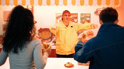 Restaurant coworker with yellow shirt and red cap dancing while service customer. Professional waiter moving to music with lively tone while looking at diverse people enjoy eating food. Regalement.