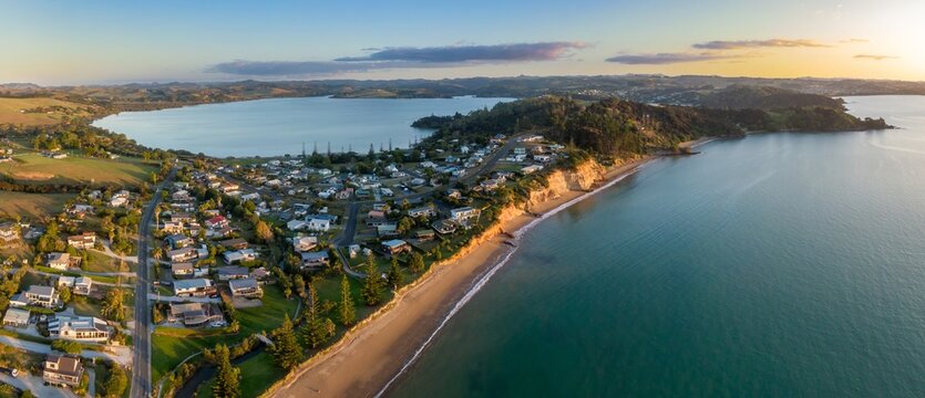 Coastal town of Hihi at sunrise, houses lining a beach. Tranquil morning light over the water. Aerial view.  Northland, NZ