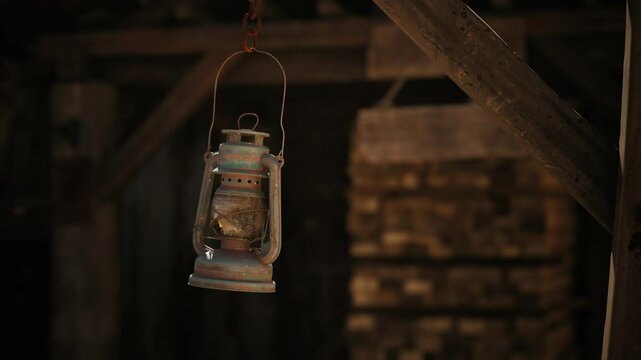 A rustic lantern hangs from the ceiling of an old barn, casting a warm glow in the dim space filled with wooden beams. The ambiance evokes a sense of nostalgia and tranquility.