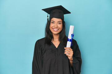 Filipina graduate with diploma on blue studio happy, smiling and cheerful.
