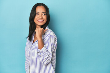 Fototapeta premium Filipina young woman on blue studio points with thumb finger away, laughing and carefree.