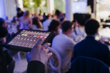 Obraz premium View of lighting technician with tablet, operator controlling sound and light during live event concert on stage show broadcast, technician with professional equipment, working on mixing console