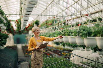 Happy old florist with clipboard in hothouse counting flowers and plants