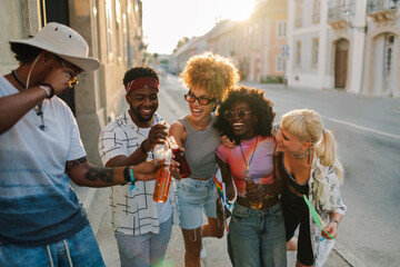 Happy friends toasting with bottles of beer at sunset in the city