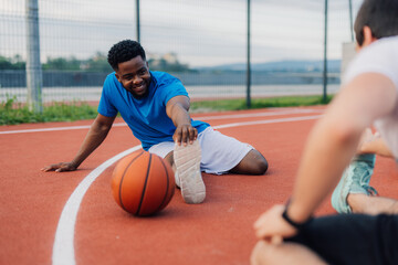 Two male basketball players stretching before training outdoors