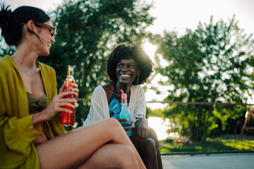 Fototapeta premium Two happy young women relaxing by the pool, enjoying refreshing drinks and good company during a sunny summer day