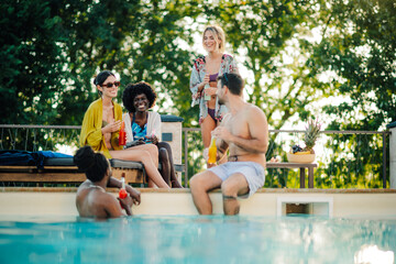 Obraz premium Friends enjoying drinks and conversation by the poolside