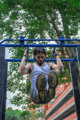 Young tattooed man doing pull-ups and parallel bars exercise in a public park surrounded by nature