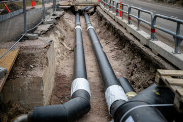 Large black underground pipes being installed in an excavated trench at a construction site,...