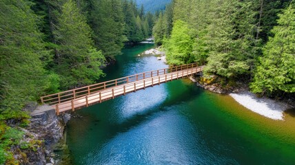 Fototapeta premium Wooden bridge over tranquil forest river surrounded by lush greenery and mountains