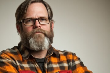 Obraz premium Portrait of a man with glasses and a beard wearing a plaid shirt against a neutral backdrop