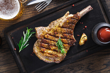 Grilled pork tomahawk steak on wooden cutting board garnished with rosemary sprigs above