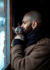 Obraz premium A man holding a cat in his arms by a window
