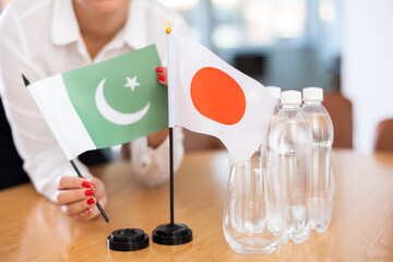 Closeup of national flags of Pakistan and Japan in hands of female office secretary preparing table in meeting room for international negotiations, selective focus. Concept of diplomatic partnerships
