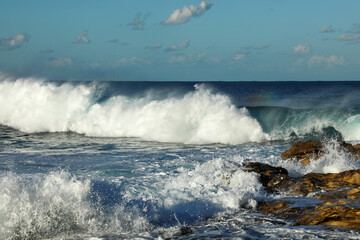 Huge waves on a rocky seashore crashing with splashes on the shore on a beautiful sunny day.
