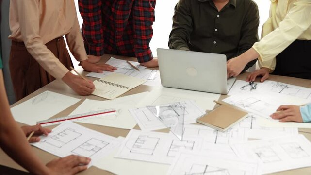 Architect and safety engineer discussion about building blueprint displaying on laptop on table with architectural document and wooden block scatter around at modern office. Closeup. Delineation.