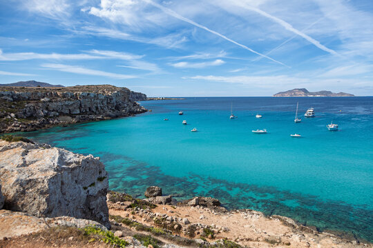 Cala Rossa Bay on Favignana Island, Sicily, with turquoise waters, anchored boats, rocky limestone cliffs, and a scenic Mediterranean backdrop under a clear sky - Powered by Adobe