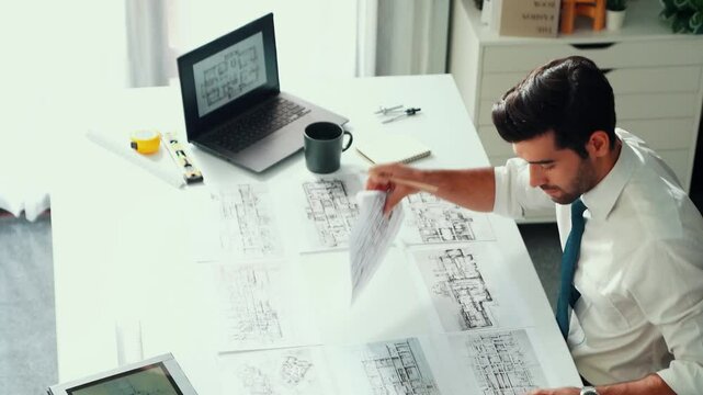 Architect engineer using laptop planning house design at office while sitting at meeting table with blueprint and equipment scatter around.Skilled civil engineer working at blueprint. Alimentation.