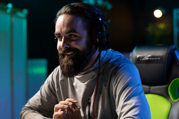 Man in neon lit apartment having fun and laughing while playing entertaining videogame with friends. Pro gamer chuckling at teammates jokes while gaming together on desktop PC