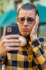 Shocked young man using smartphone typing browsing, loses becoming surprised sudden lottery...