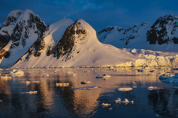 Antarctic Peninsula: Snowy peaks, icebergs, cloudy sky. Lemaire Channel