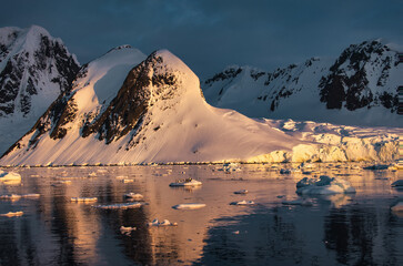 Antarctic Peninsula: Snowy peaks, icebergs, cloudy sky. Lemaire Channel