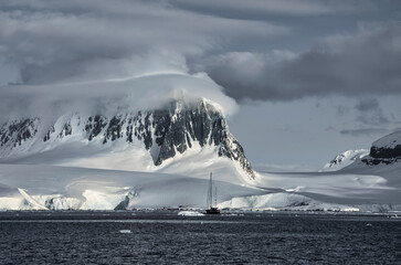 Antarctic Peninsula: Snowy peaks, icebergs, cloudy sky. Lemaire Channel