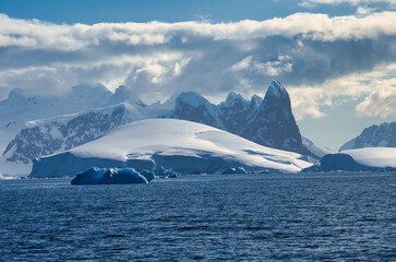 Antarctic Peninsula: Snowy peaks, icebergs, cloudy sky. Lemaire Channel