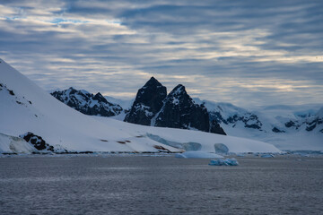 Antarctic Peninsula: Snowy peaks, icebergs, cloudy sky. Lemaire Channel