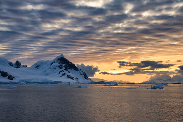 Antarctic Peninsula: Snowy peaks, icebergs, cloudy sky. Lemaire Channel