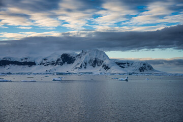 Antarctic Peninsula: Snowy peaks, icebergs, cloudy sky. Lemaire Channel
