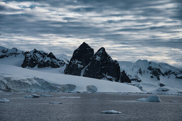 Antarctic Peninsula: Snowy peaks, icebergs, cloudy sky. Lemaire Channel
