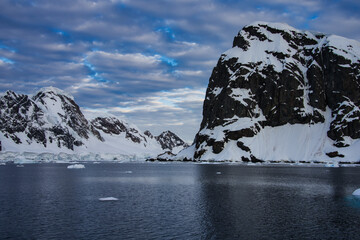 Antarctic Peninsula: Snowy peaks, icebergs, cloudy sky. Lemaire Channel
