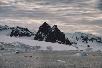 Antarctic Peninsula: Snowy peaks, icebergs, cloudy sky. Lemaire Channel